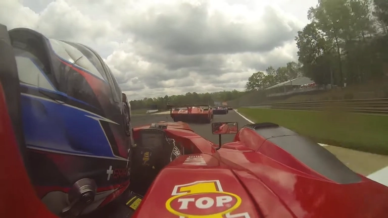 A driver is wearing a helmet and is in the cockpit of a single-seater car customized with Top 1 logo