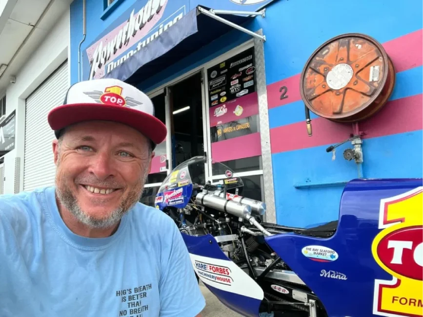a man smiling standing next to his motorcycle customized with Top 1 logo