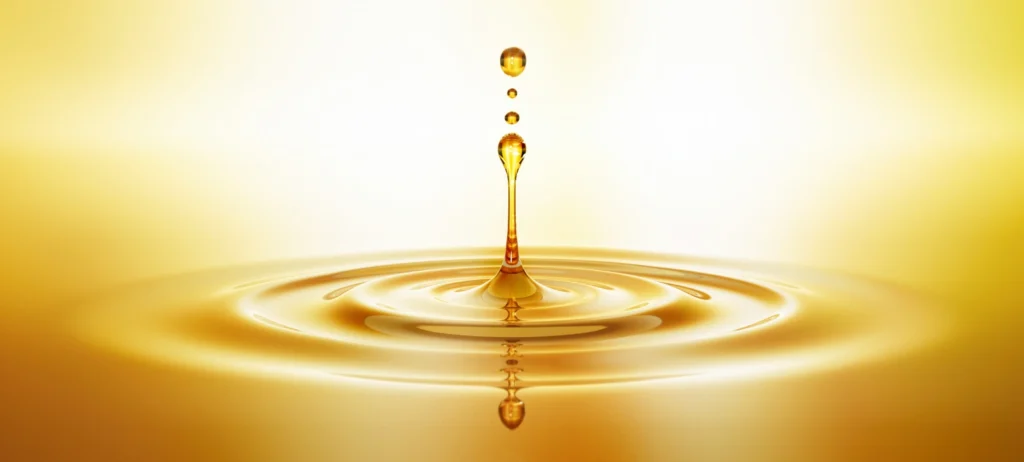 Golden oil drop falling into a smooth liquid surface creating ripples in warm light